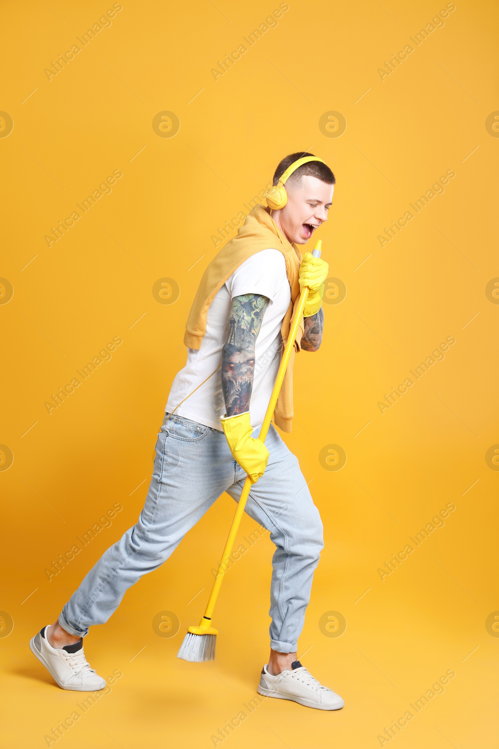 Photo of Handsome young man with floor brush singing on orange background