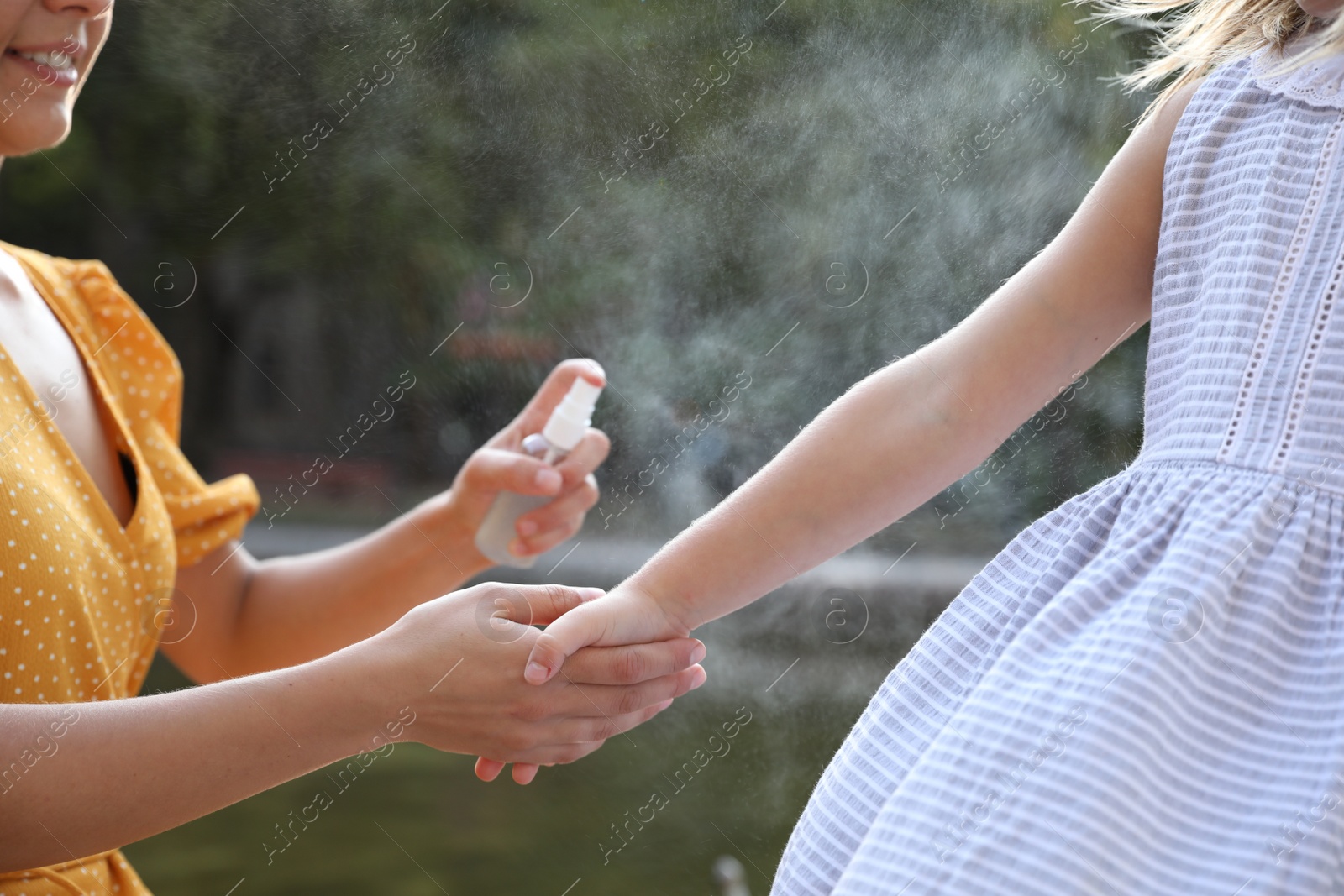 Photo of Mother applying insect repellent onto girl's hand outdoors, closeup