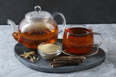 Photo of Aromatic licorice tea, dried sticks of licorice root and powder on light gray textured table