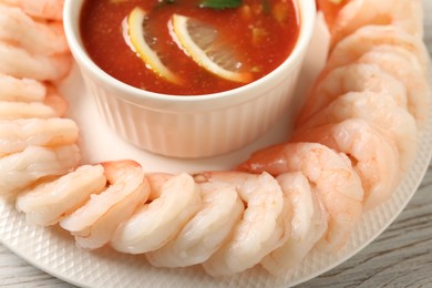 Tasty boiled shrimps with cocktail sauce and lemon on white wooden table, closeup