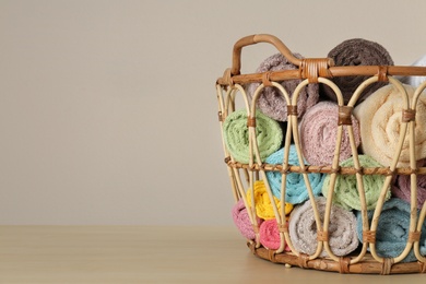 Wicker basket with clean soft towels on wooden table. Space for text