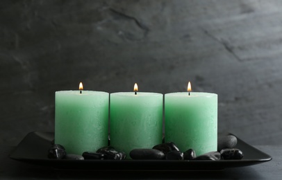 Dark plate with three burning candles and rocks on table