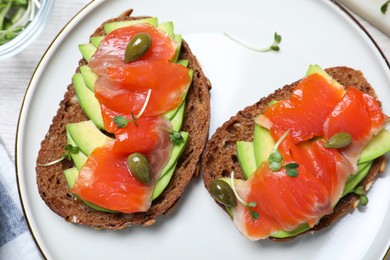 Photo of Delicious sandwiches with salmon, avocado and capers on plate, top view