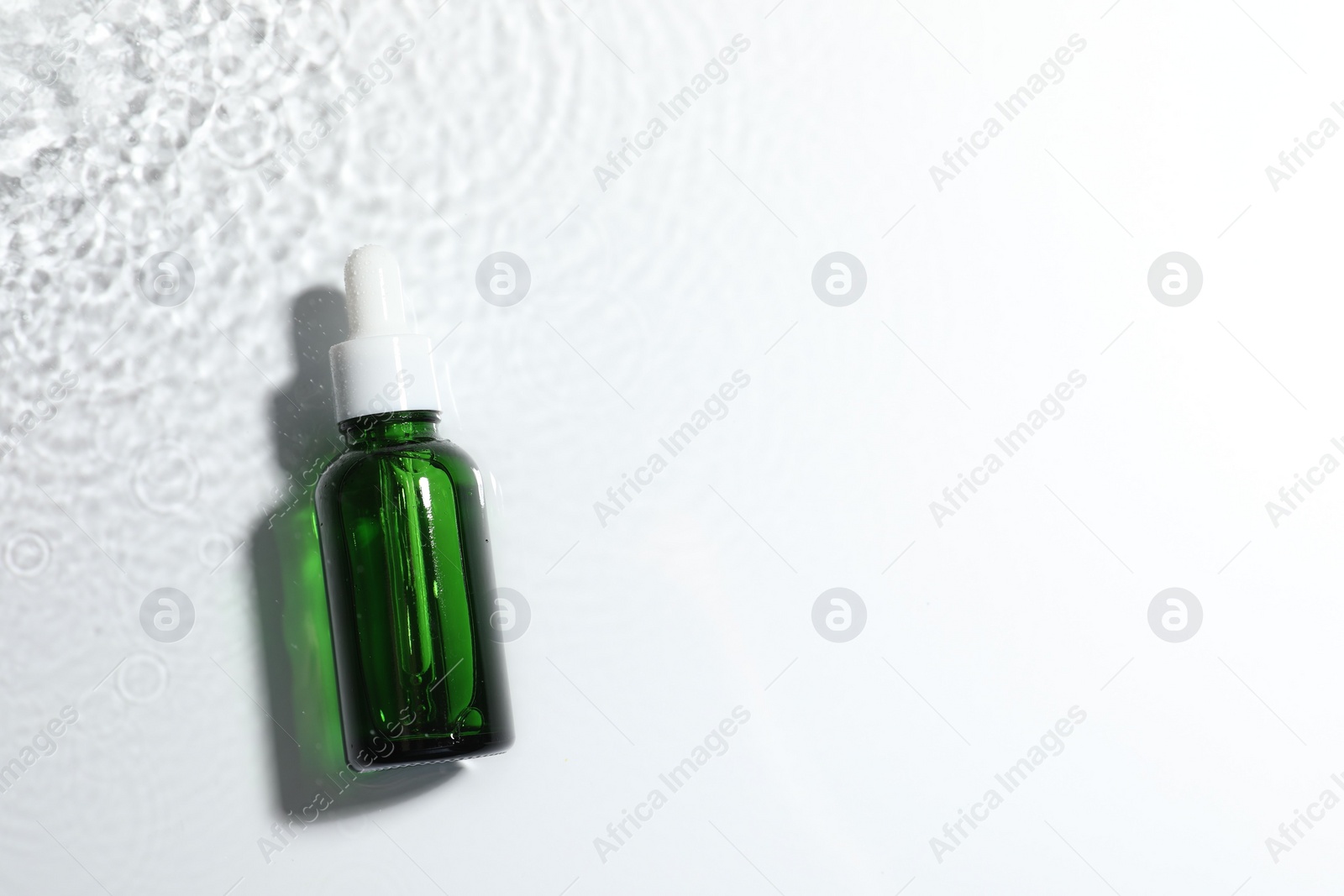 Photo of Bottle of cosmetic product in water on white background, top view. Space for text