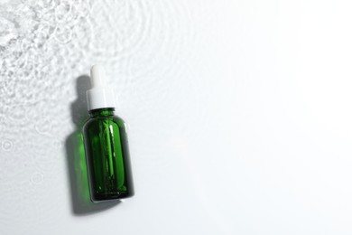 Bottle of cosmetic product in water on white background, top view. Space for text