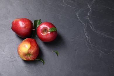 Photo of Ripe red apples and leaves on black textured table, flat lay. Space for text