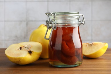 Photo of Tasty homemade quince jam in jar and fruits on wooden table, closeup