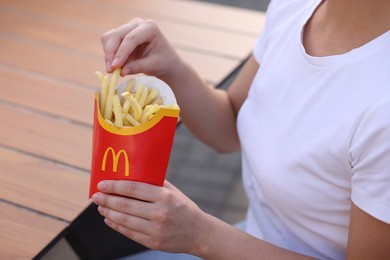 Photo of Lviv, Ukraine - September 26, 2023: Woman with McDonald's French fries at wooden table outdoors, closeup