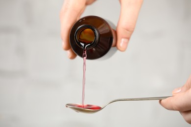 Photo of Woman pouring cough syrup into spoon on light background, closeup