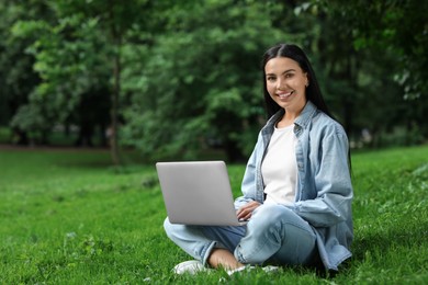 Photo of Happy young woman using modern laptop on green grass in park. Space for text