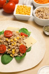 Photo of Delicious tortilla with tuna, vegetables and cheese on light table, closeup. Cooking shawarma