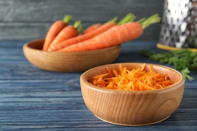 Photo of Bowl of grated carrot on wooden table. Space for text