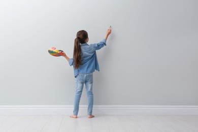 Little girl painting on light grey wall indoors, back view. Space for text