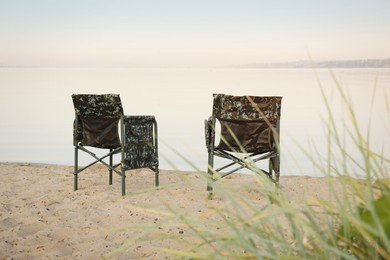 Camouflage fishing chairs on sandy beach near river