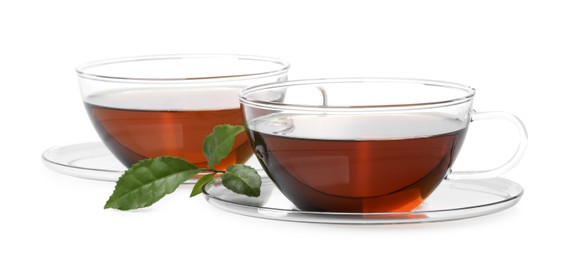 Glass cups of hot aromatic tea and green leaves on white background