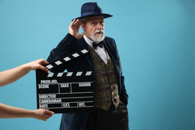 Photo of Senior actor performing role while second assistant camera holding clapperboard on light blue background, space for text. Film industry