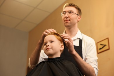 Photo of Professional hairdresser working with boy in beauty salon, low angle view