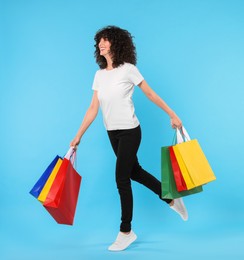 Photo of Happy young woman with shopping bags on light blue background