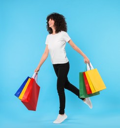 Happy young woman with shopping bags on light blue background