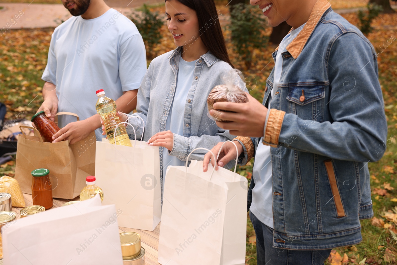 Photo of Group of volunteers packing food products at table in park, closeup