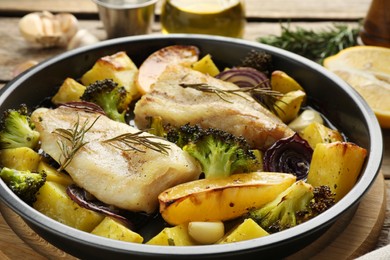 Photo of Pieces of delicious baked cod with vegetables, lemon and spices in dish on table, closeup