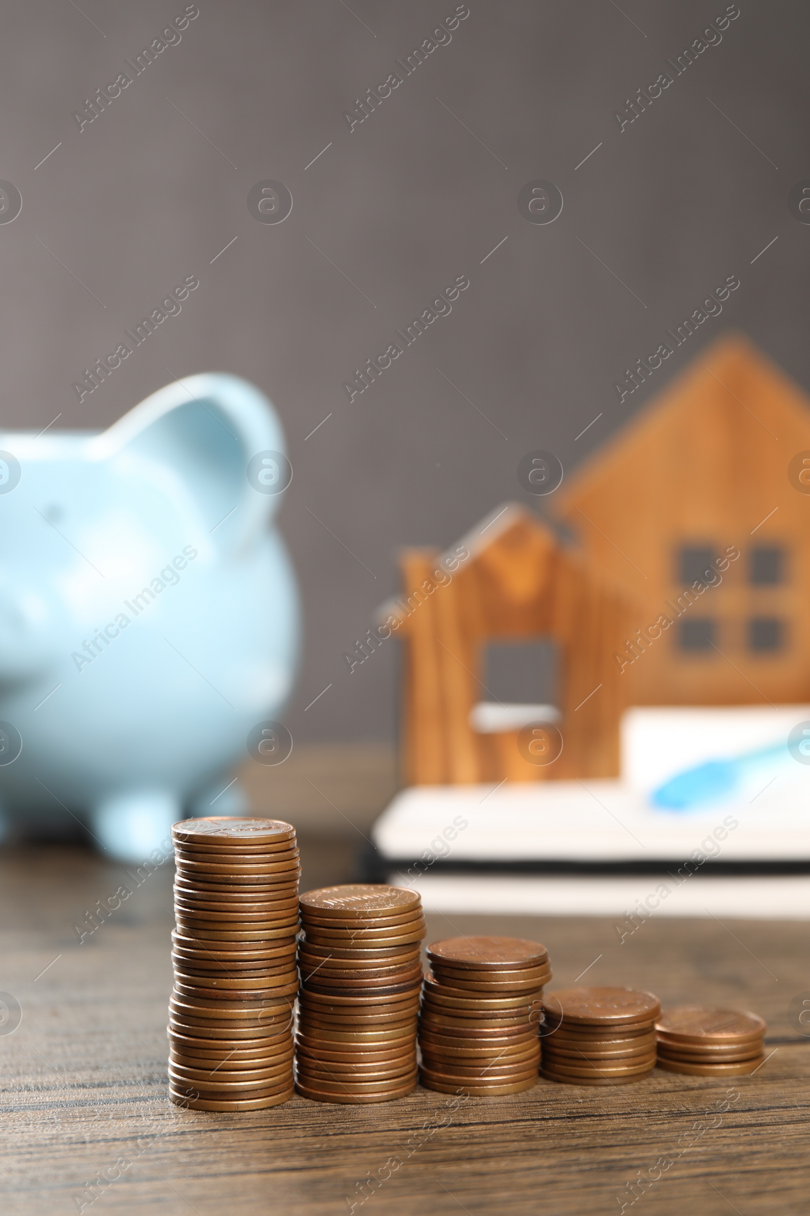 Photo of House models, stacked coins, piggy bank and notebook on wooden table, selective focus