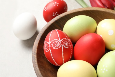 Bowl with painted Easter eggs on light background, closeup