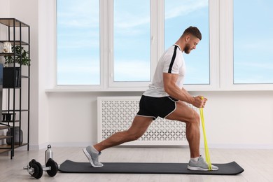 Athletic man doing exercise with elastic resistance band on mat at home