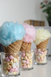 Photo of Sweet cotton candies in waffle cones and marshmallows on white table indoors, closeup