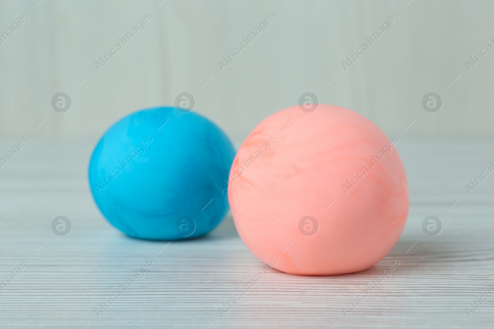 Photo of Different color play dough balls on white wooden table, closeup