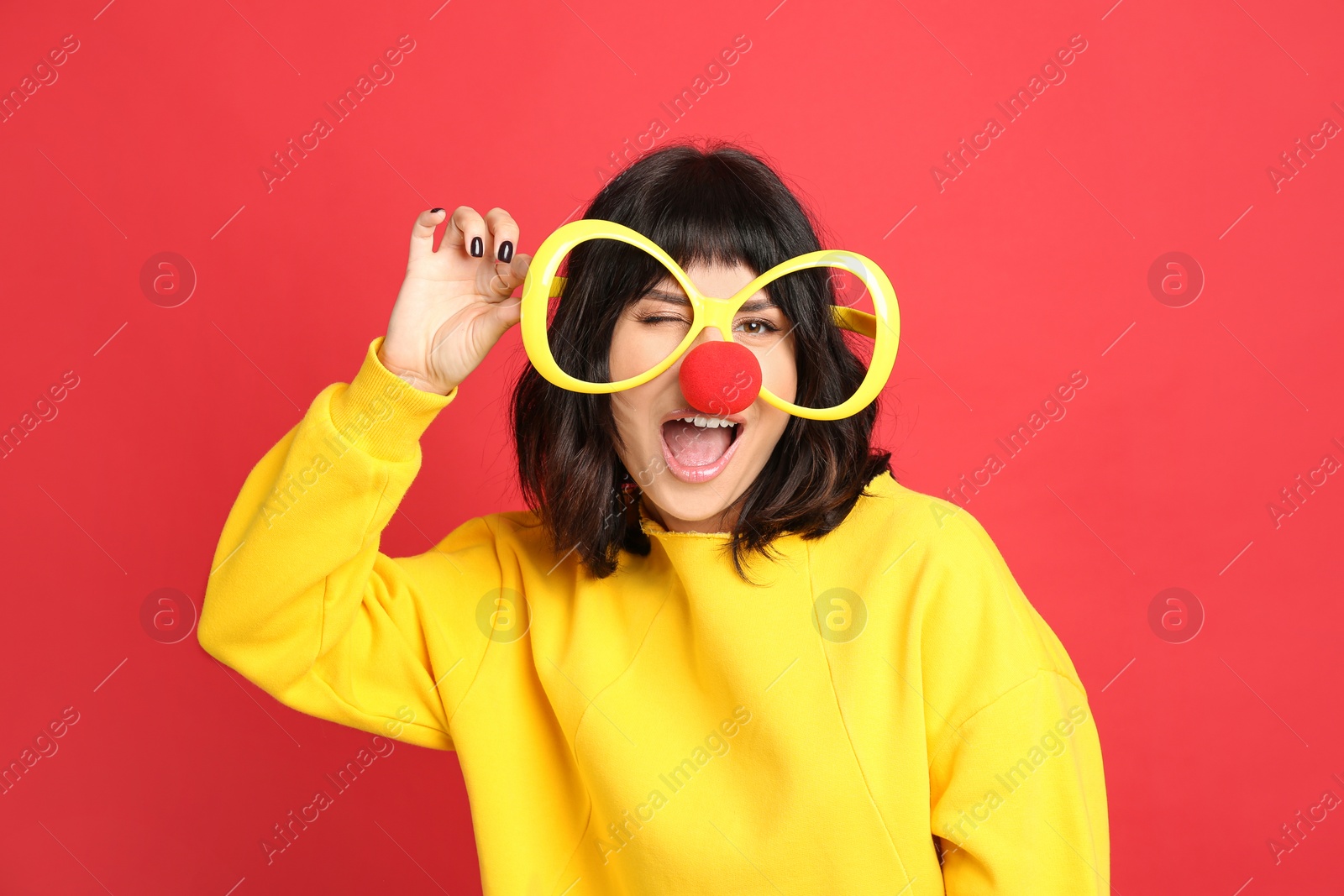 Photo of Joyful woman with large glasses and clown nose on red background. April fool's day