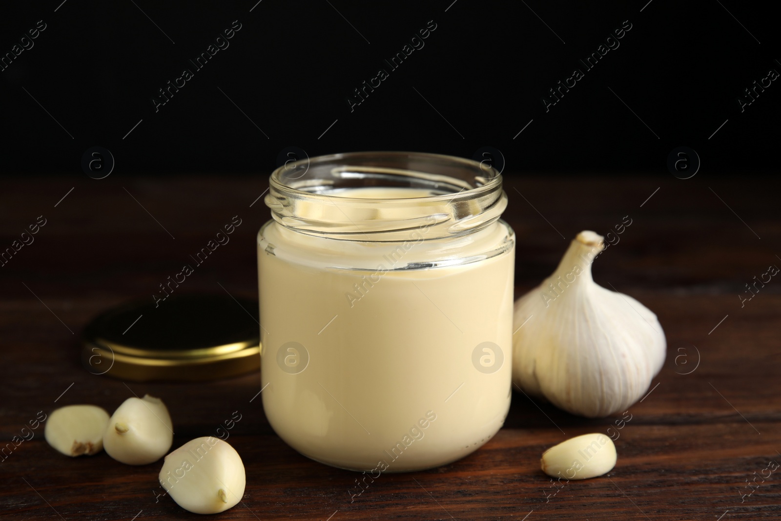 Photo of Jar of delicious mayonnaise and fresh garlic on wooden table