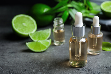 Lime essential oil and cut citrus fruits on grey table. Space for text