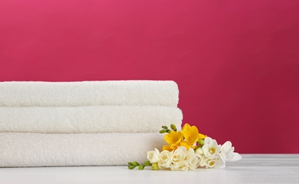 Photo of Stack of soft clean towels with beautiful flowers on table against color background. Space for text