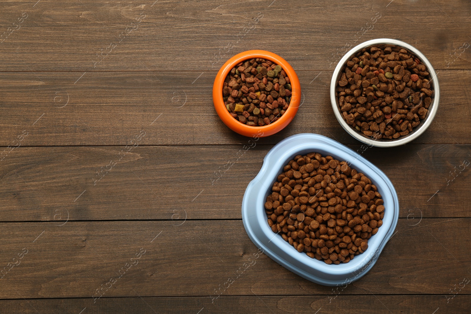 Photo of Dry food in pet bowls on wooden background, flat lay. Space for text