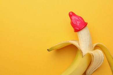 Photo of Banana with condom on orange background, top view and space for text. Safe sex concept