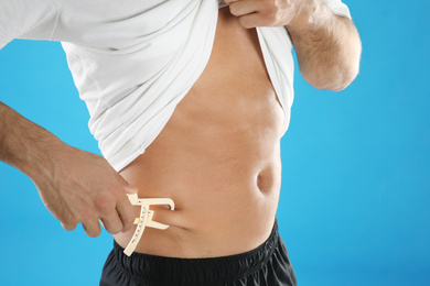 Photo of Man measuring body fat layer with caliper on light blue background, closeup. Nutritionist's tool