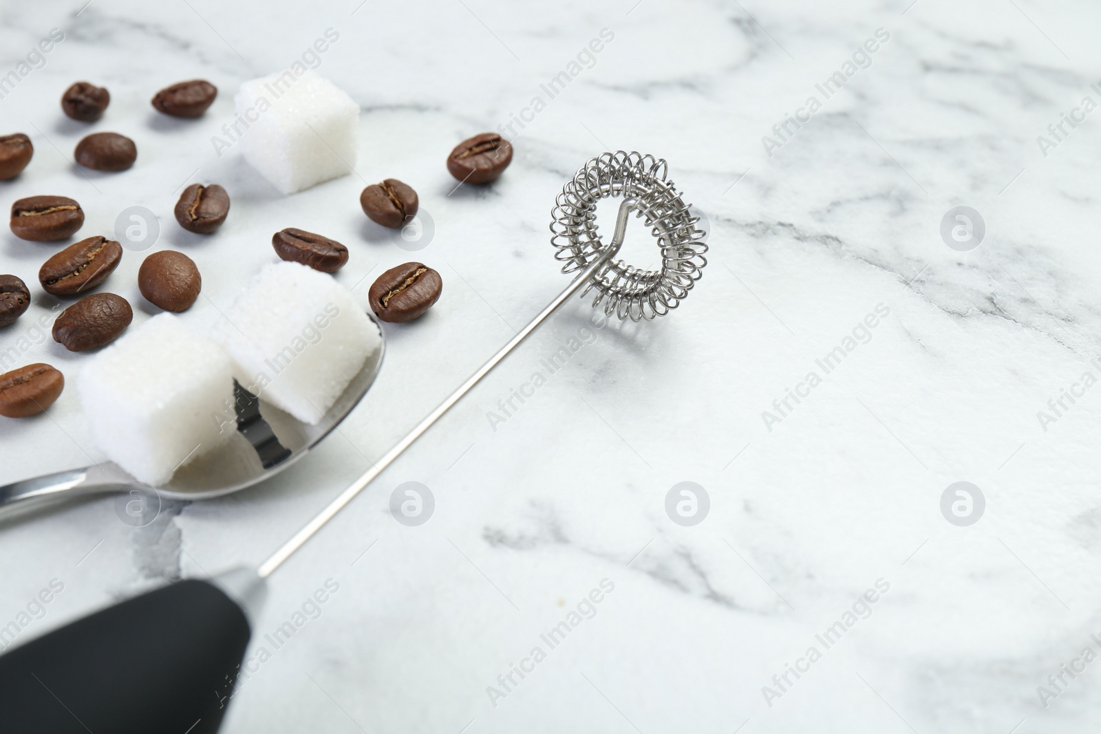 Photo of Black milk frother wand, sugar cubes and coffee beans on white marble table, closeup. Space for text