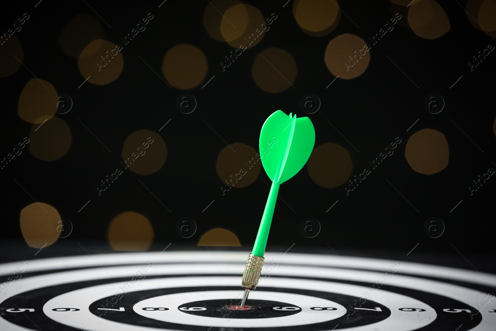 Photo of Green arrow hitting target on dart board against blurred lights