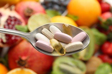 Different vitamin pills in spoon over fresh fruits, top view