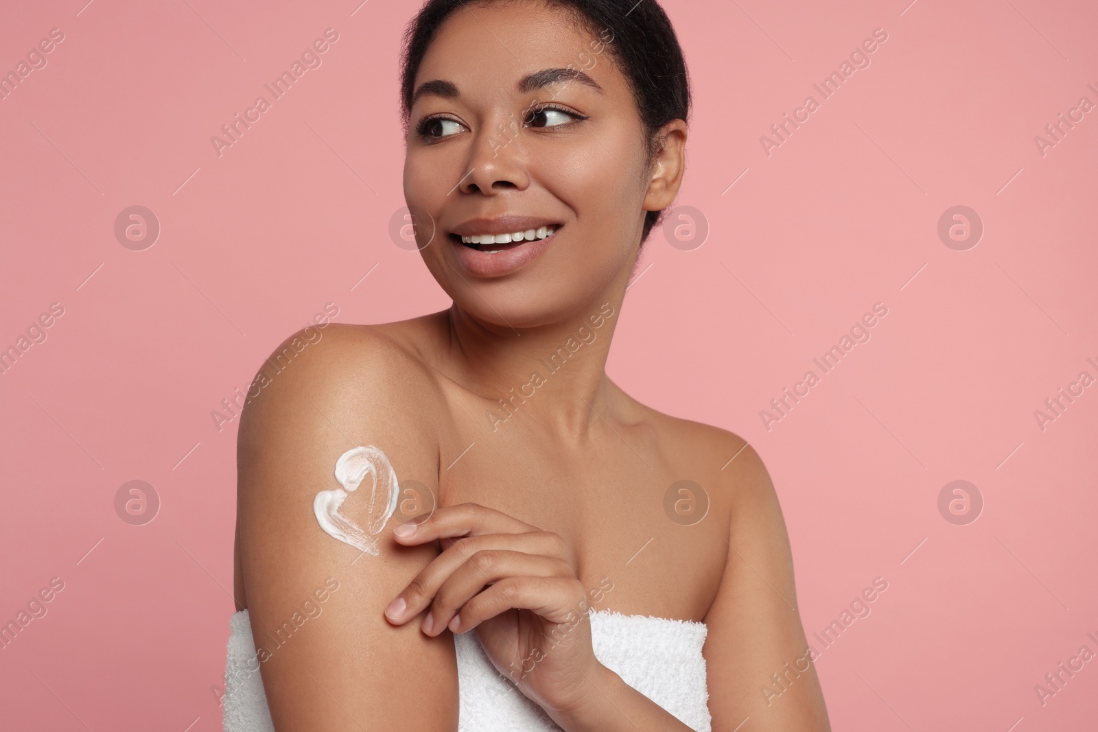 Photo of Young woman applying body cream onto arm on pink background