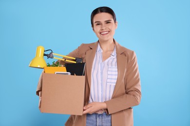 Photo of Happy unemployed woman with box of personal office belongings on light blue background