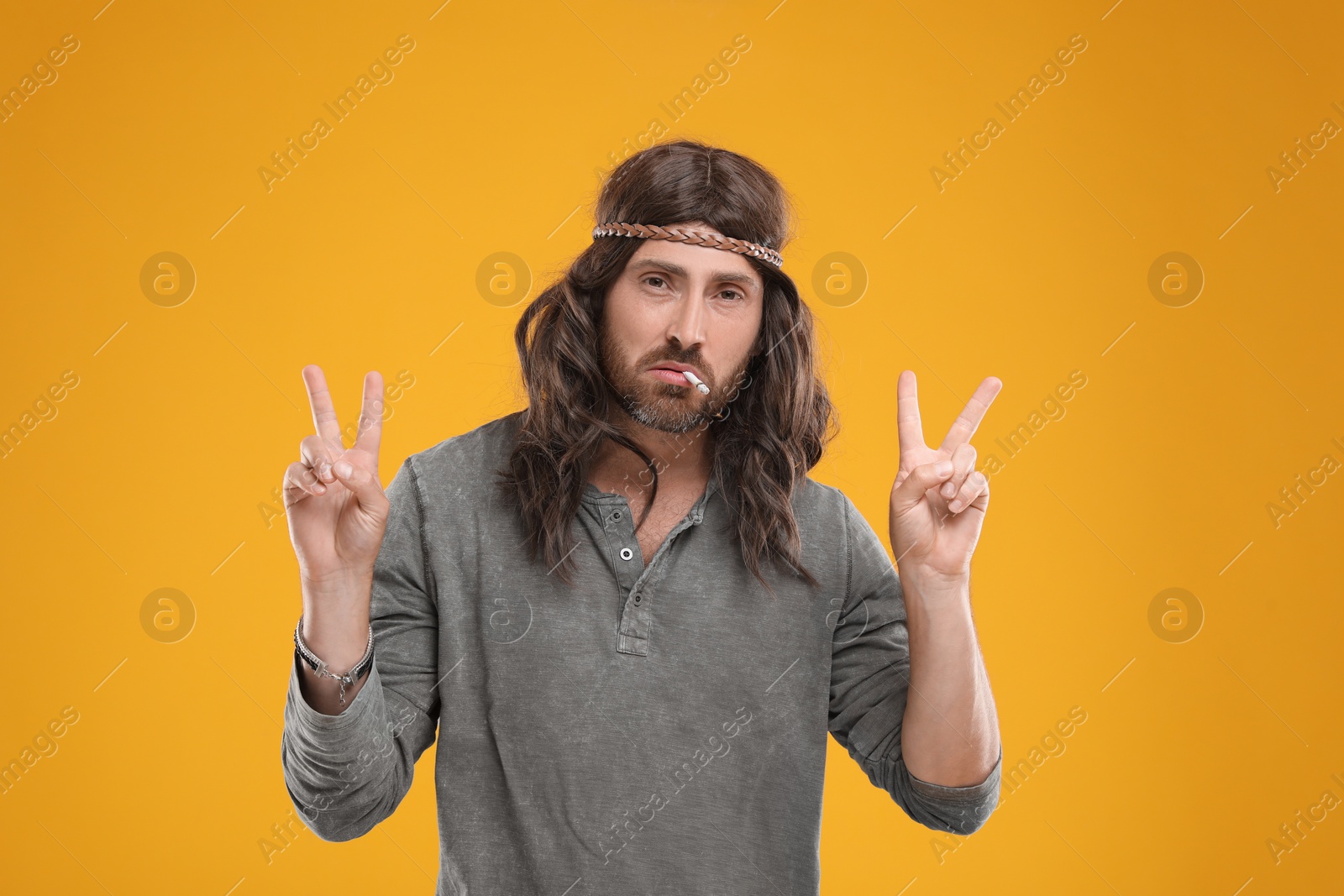 Photo of Hippie man smoking cigarette and showing V-sign on orange background