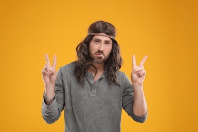 Photo of Hippie man smoking cigarette and showing V-sign on orange background