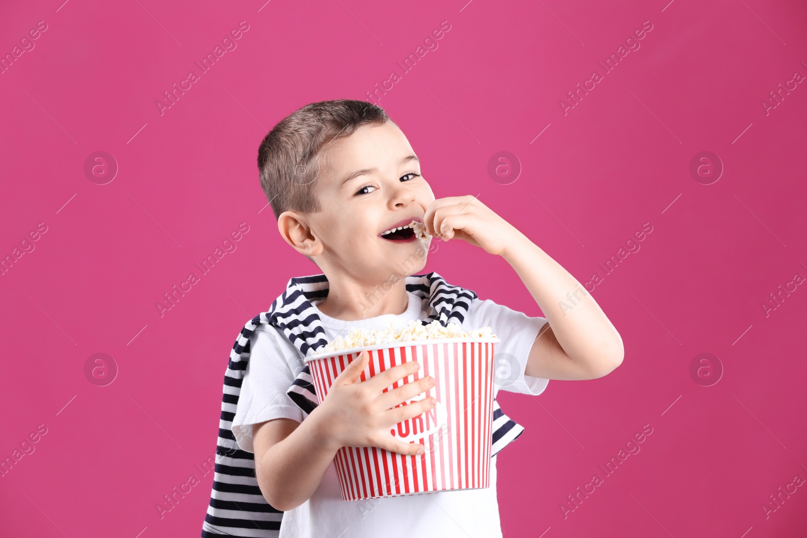 Photo of Cute little boy with popcorn on color background