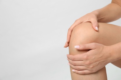 Woman having knee problems on grey background, closeup with space for text