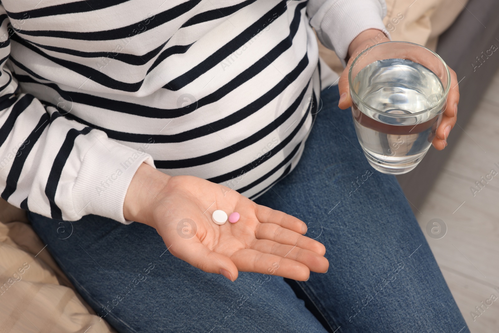 Photo of Pregnant woman with glass of water and pill at home, closeup