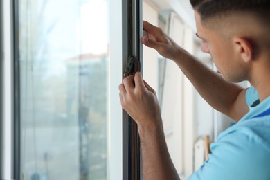 Photo of Man putting rubber draught strip onto window indoors, focus on hands