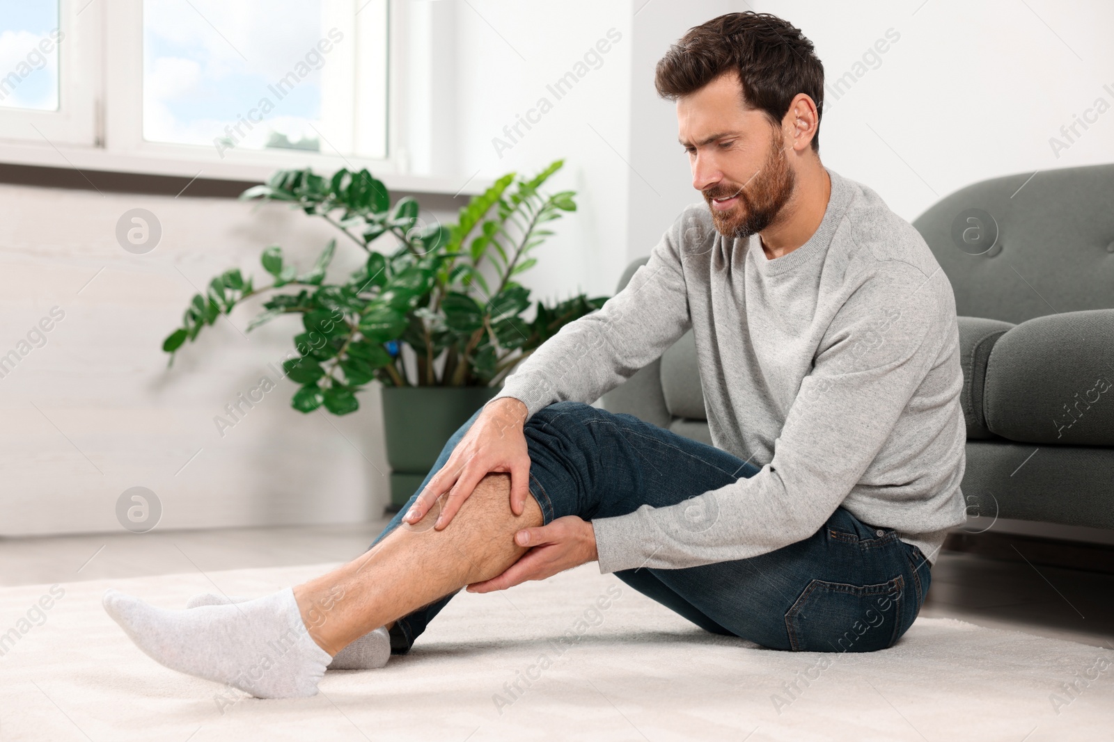 Photo of Man suffering from leg pain near sofa in room