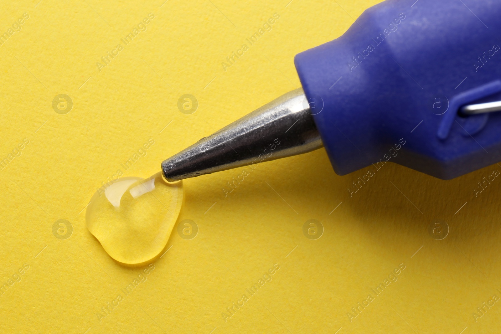 Photo of Melted glue dripping out of hot gun nozzle on yellow background, closeup